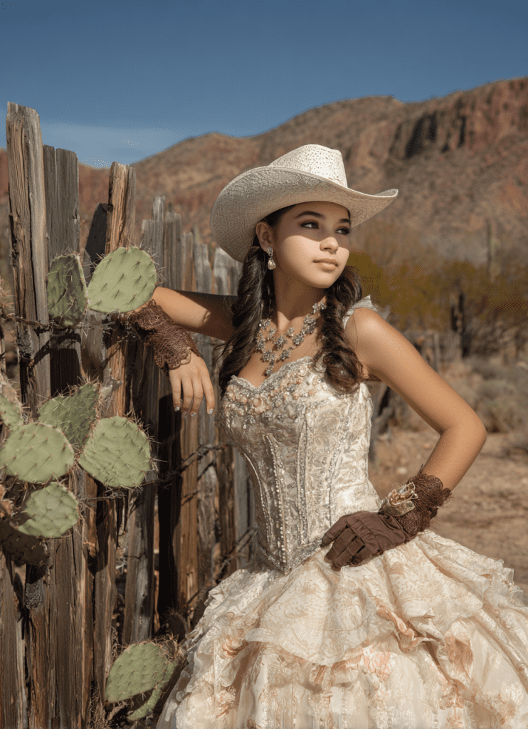 Quinceañera celebrating at Cocoraque Ranch in Tucson, wearing a sparkling gown and cowboy hat by a rustic fence with cactus and desert mountains.