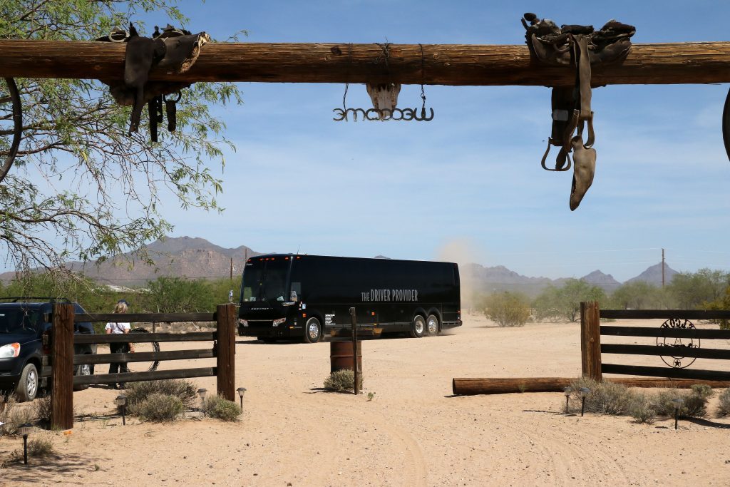 A tour bus arriving at Cocoraque Ranch under a rustic wooden entrance gate in Marana, Tucson, Arizona.
