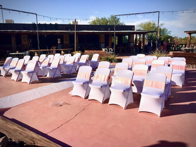 Outdoor ceremony seating with white chair covers and blush sashes under string lights at Cocoraque Ranch in Marana, AZ