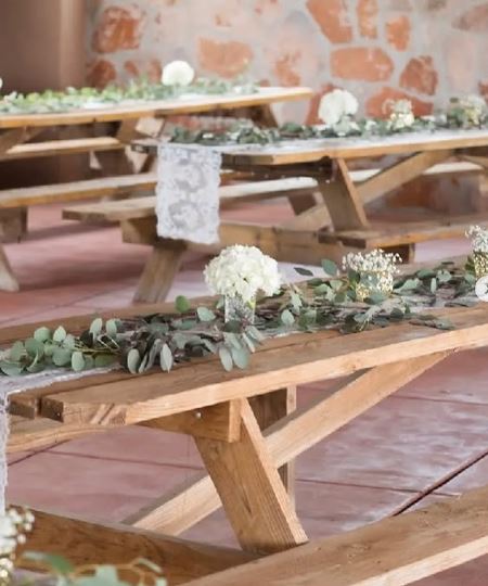 Rustic wooden picnic tables decorated with greenery and white flowers at Cocoraque Ranch wedding venue near Tucson.